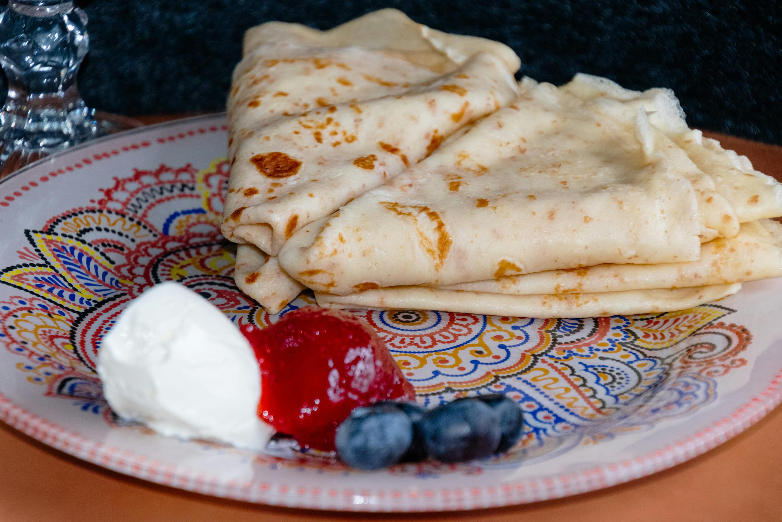 Tasty crepes served with blueberries, strawberries, and cream on a vibrant patterned plate.